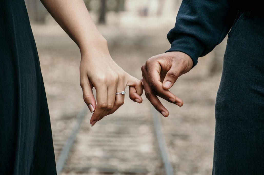 Married couple holding hands while walking on railroad tracks.