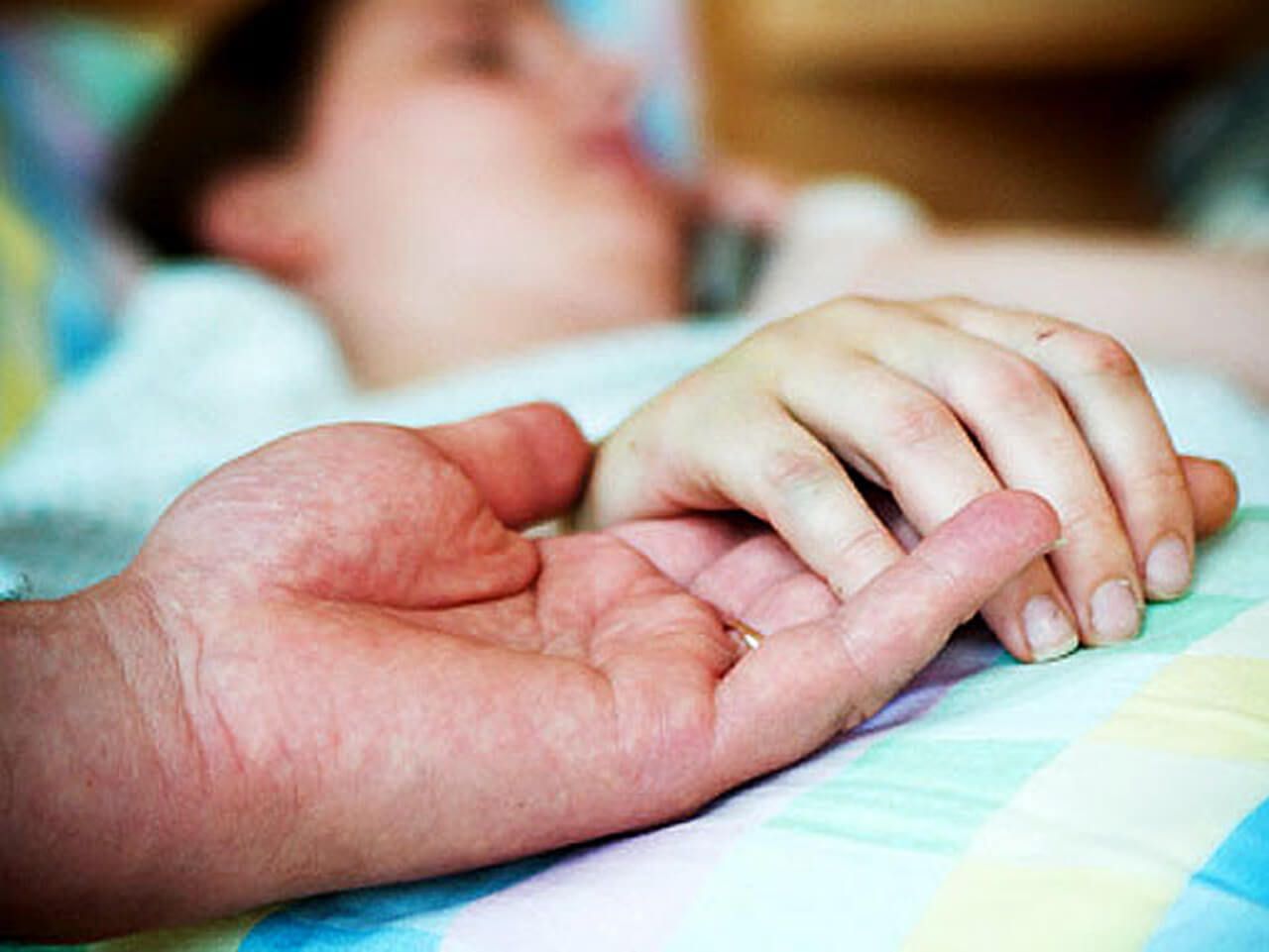 A husband holding his wife's hand while she lays in a hospital bed
